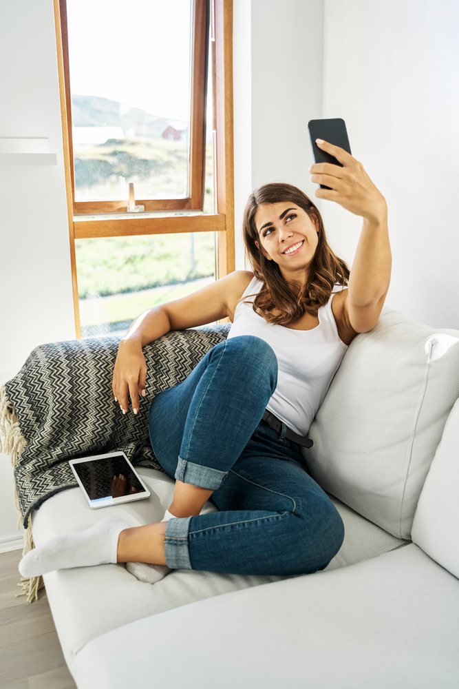 A white woman takes a selfie while relaxing on a couch