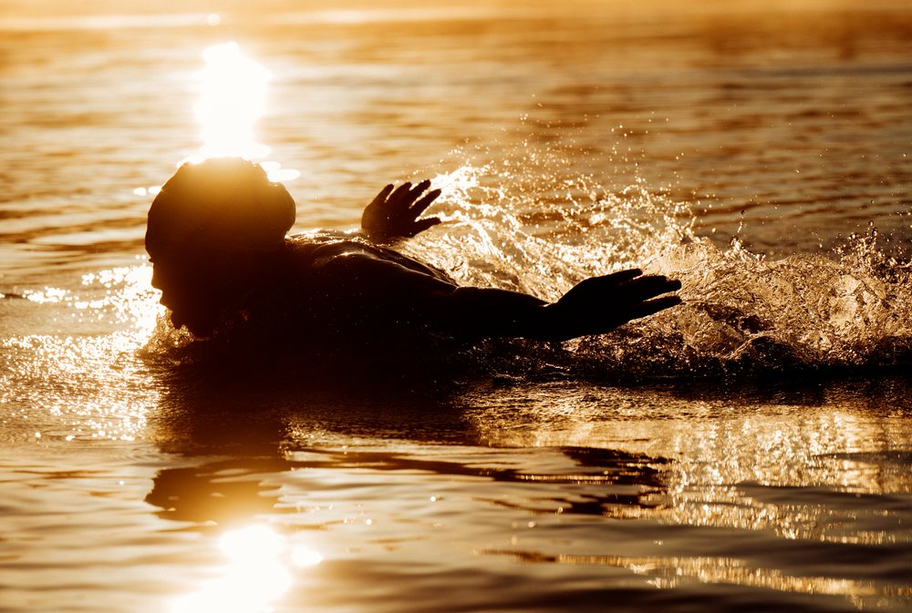 Person swimming and splashing in a lake during golden hour at sunset, USA.