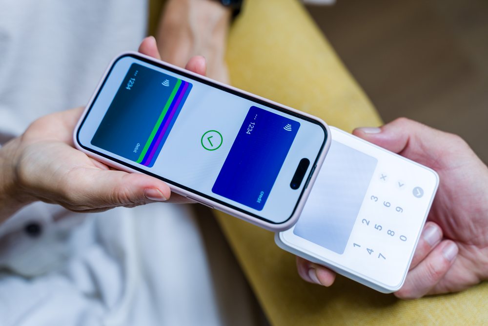 Human hand holds a smartphone displaying a digital wallet app and a white card reader during a contactless payment transaction, Spain.