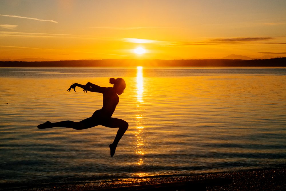 Silhouette of a person performing an acrobatic jump on the shore at sunset over a calm lake, yoga, acrobatics, USA.