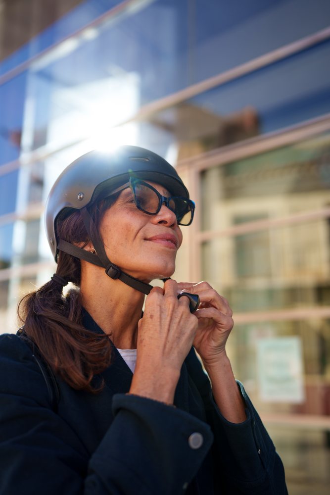 Woman outdoors fastening a black helmet strap under sunlight in an urban street setting, Málaga.