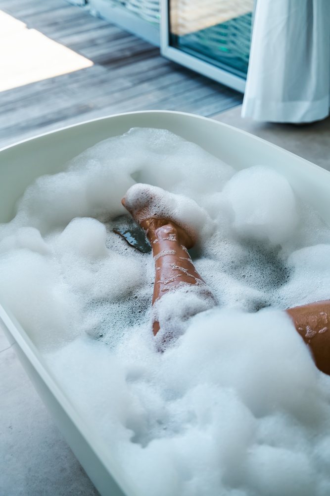 A person relaxing with legs immersed in a bubble bath inside a bathtub at a bathroom in the, Maldives.