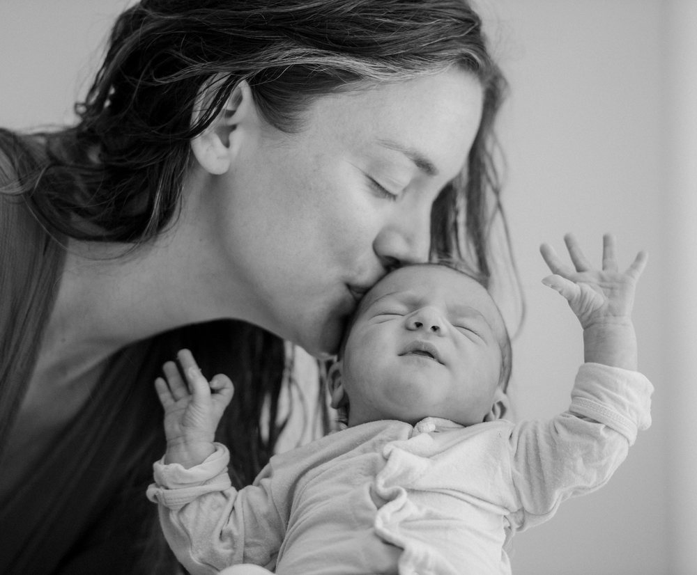 Mother tenderly kisses her newborn baby indoors in a black and white portrait conveying affection and bonding, USA.