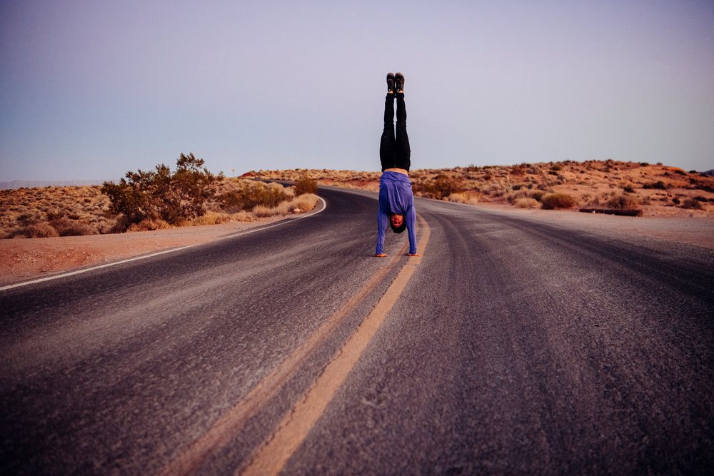 Person performing a handstand on a curved desert road at sunset, yoga, acrobatics, USA.