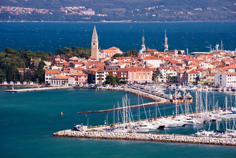 Marina and harbor of the town of Izola on the Mediterranean Sea coast with red tile roofs and church tower visible.