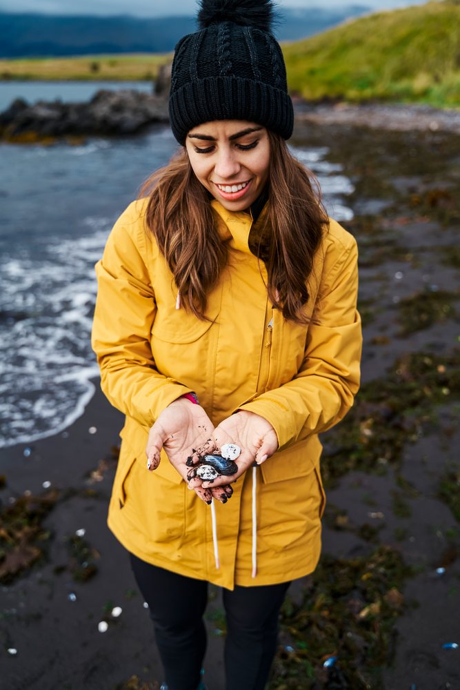 White Woman holding seashells on a black sand beach in a beach