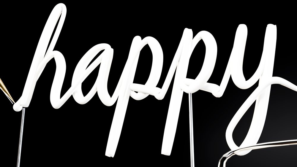 White neon sign glowing with the word happy in a calligraphic handwritten style on a black background.