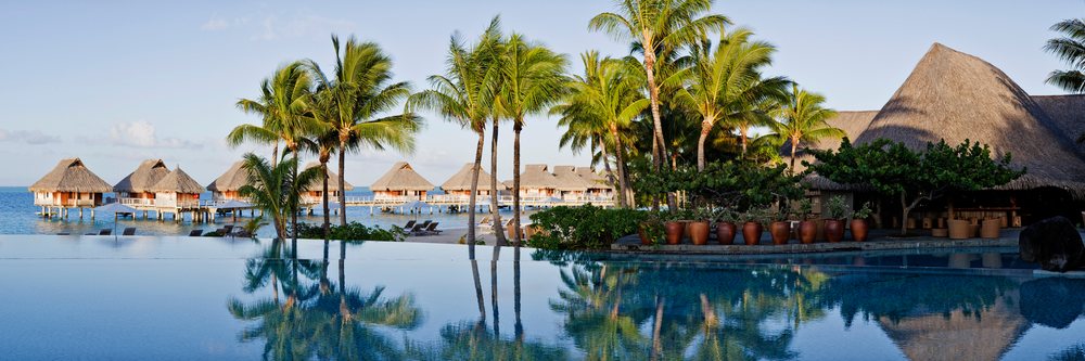 Infinity swimming pool reflecting palm trees with tropical overwater bungalows at Bora Nui Resort, Society Islands, Polynesia.
