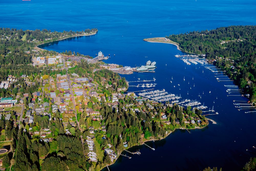 Aerial view of Bainbridge Island with Eagle Harbor showing marinas, boats, docks, and surrounding residential and forest areas on Puget Sound, Salish Sea, USA.