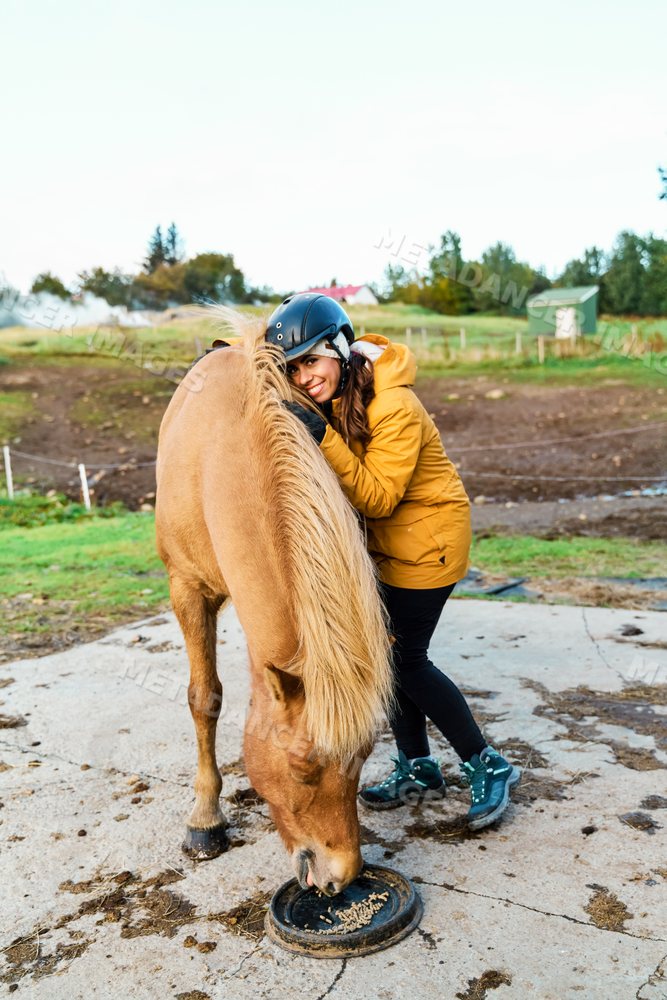 A young white woman hugs a horse feeding outdoors on a farm