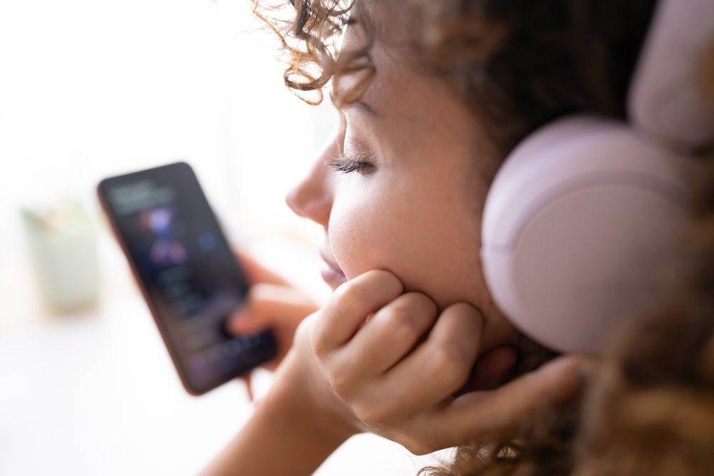 Woman with curly hair listening to music on a smartphone indoors at home, Spain.