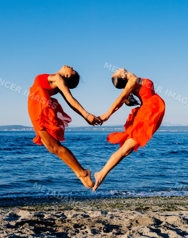 Two women in red dresses perform partner acrobatics jumping on a beach