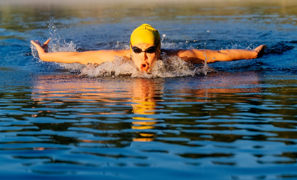 Swimmer performing the butterfly stroke in an open water lake at sunrise, USA.