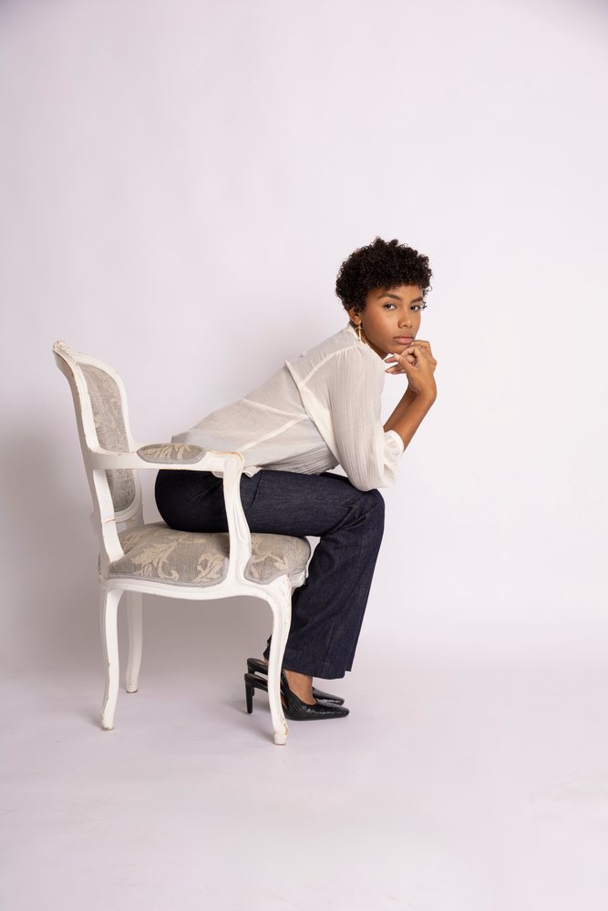 Woman sitting thoughtfully on an antique upholstered chair against a white studio background, fashion, young culture.