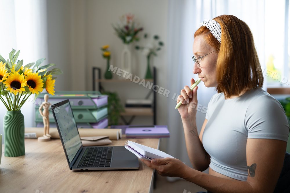 A white woman works thoughtfully in a bright home office in a office
