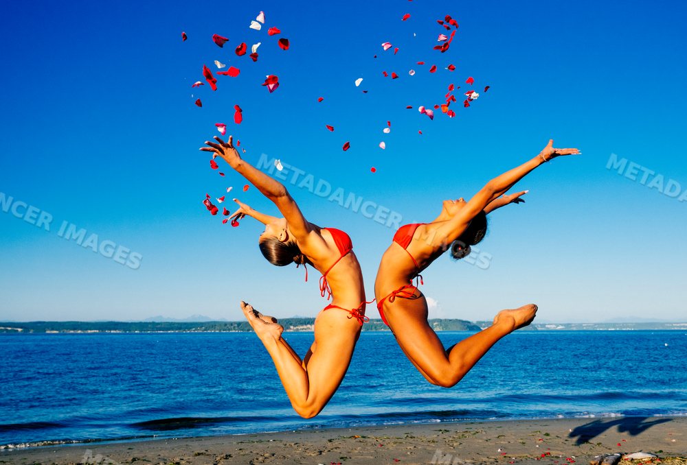 Two women practice partner acrobatics yoga jumping on a beach