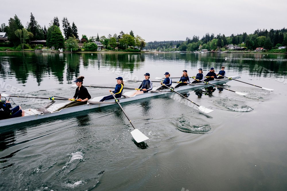 A team of eight white women rowing in unison on calm water