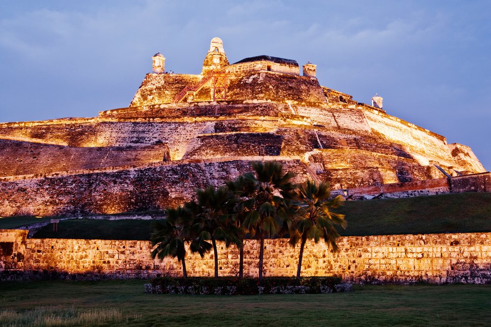 The illuminated Castillo de San Felipe de Barajas fortress at night with palm trees and grassy foreground, Colombia.