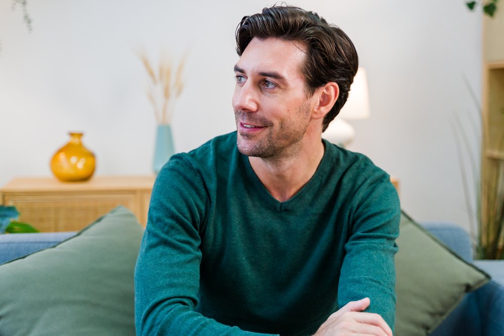 Man seated on a sofa looking away in a modern living room with cushions and décor, Spain.