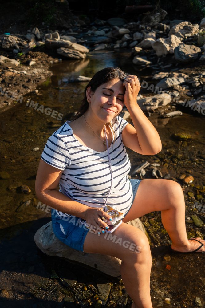 Pregnant woman relaxes by a rocky riverbank enjoying warm sunlight