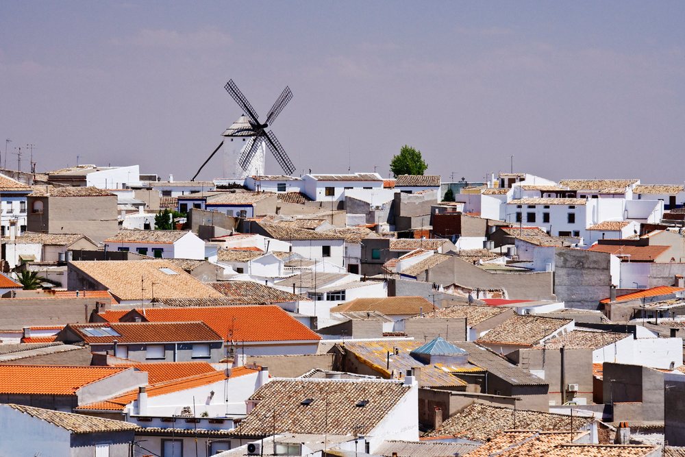 Windmill overlooks white buildings with terracotta roofs in the village of La Mancha on a clear day, Spain.