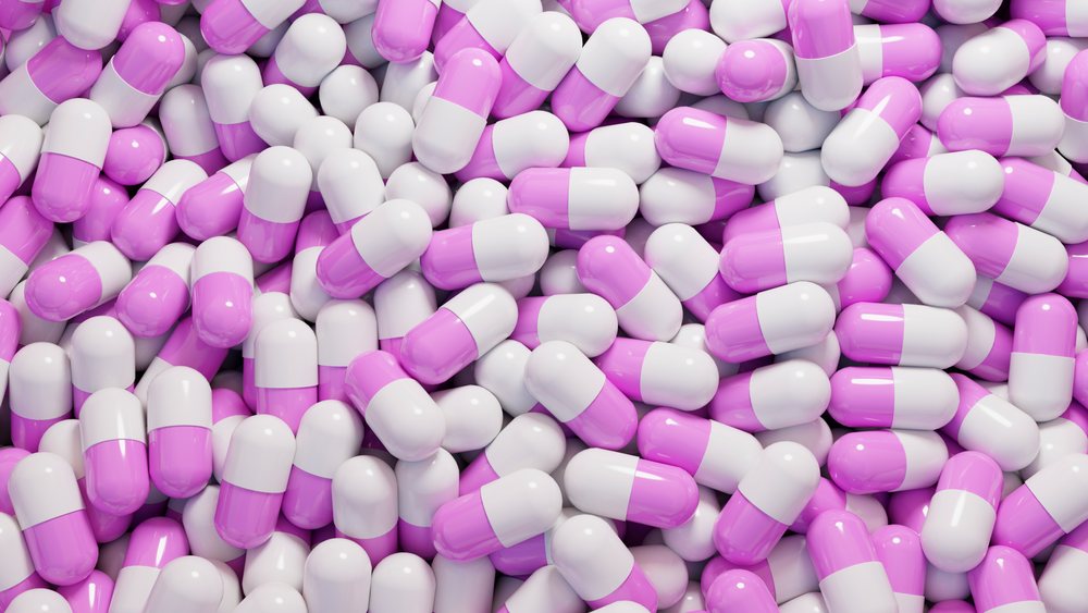 Pink and white capsule pills closely packed forming a pile representing medication and pharmaceutical treatment.