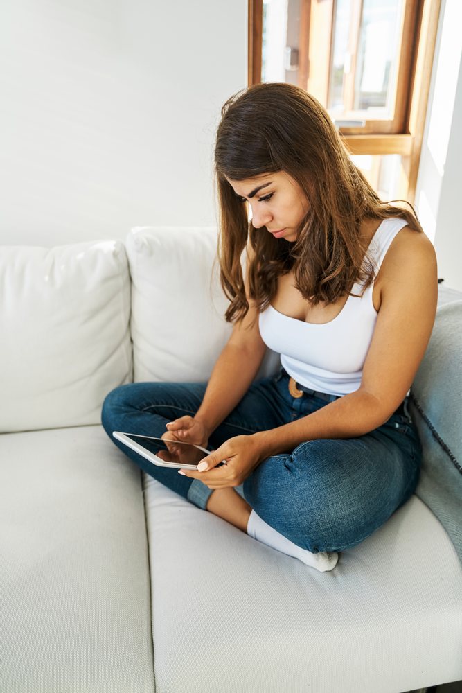A woman sits on a white couch using a tablet in a bright Iceland home