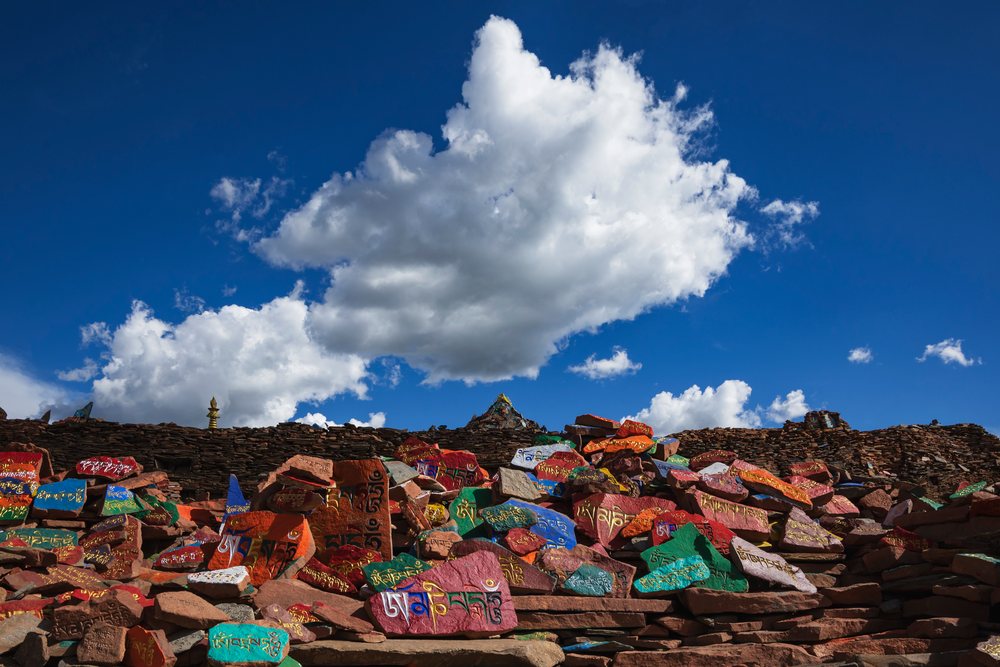 Mani Wall of colorful painted stones inscribed with Tibetan script at Songge Mani Shijingcheng, China under a blue sky with clouds, Dangkuai, Sichuan Province, People's Republic of China.
