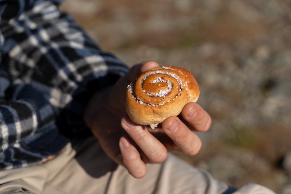 Hand holding a cinnamon roll topped with sugar crystals outdoors, Norway.