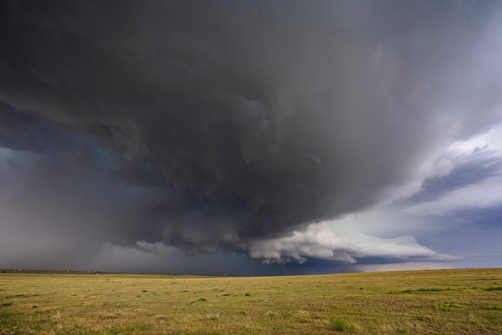 Large dark supercell thunderstorm cloud forms over open grassy plains, in Tornado Alley with distant wind turbines visible, Storm Chasing, Weather, Environmental Issues, Genoa, Colorado, USA.