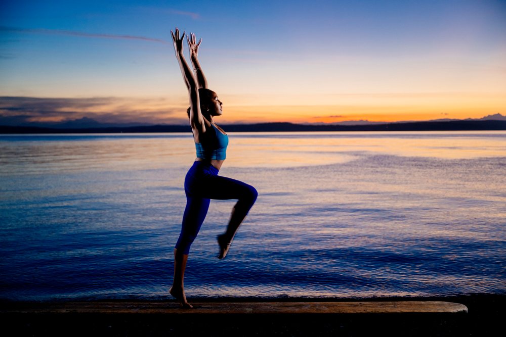 Woman performing an acrobatic yoga pose on the shore at sunset, USA.