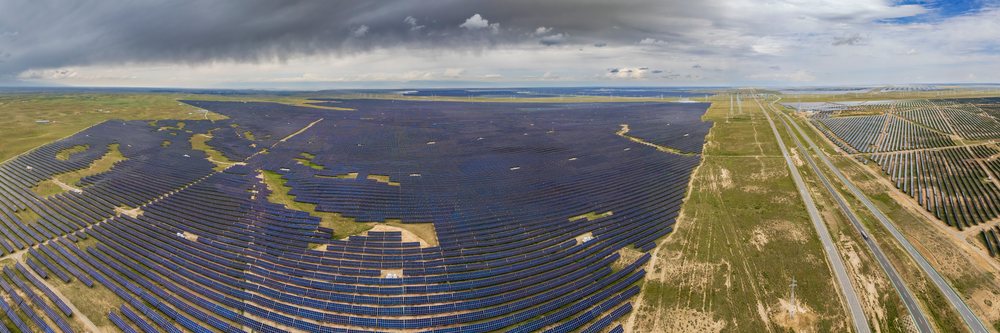 Large solar farm with panels stretching across a field beside a road under cloudy skies, Hainan - Xinghai, Qinghai Provinca, Anduo Tibet.