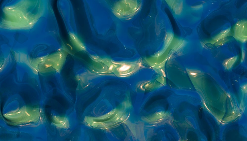 Abstract colorful liquid surface with shiny reflections in blue and green tones.