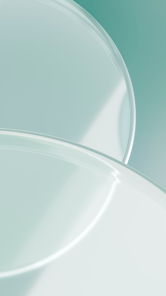 Two transparent round plates overlap with smooth glass surfaces on a soft green background showing gentle reflections.
