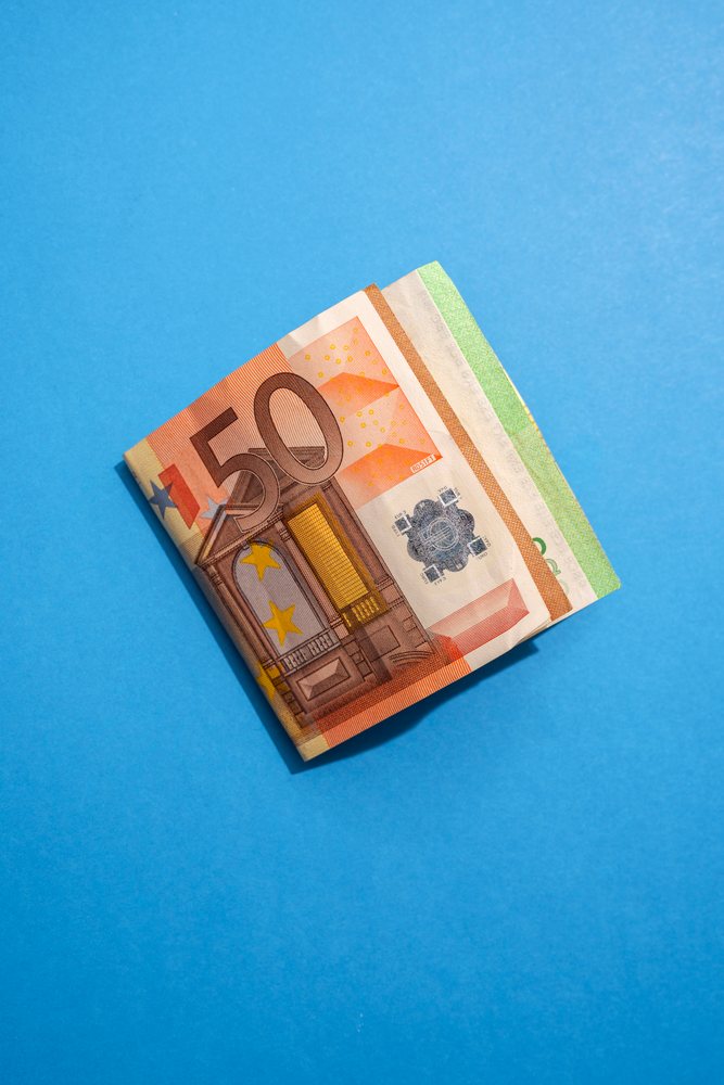 Stack of euro banknotes with a 50 euro note on top and a partially visible 10 euro note on a blue background, Studio Shot.