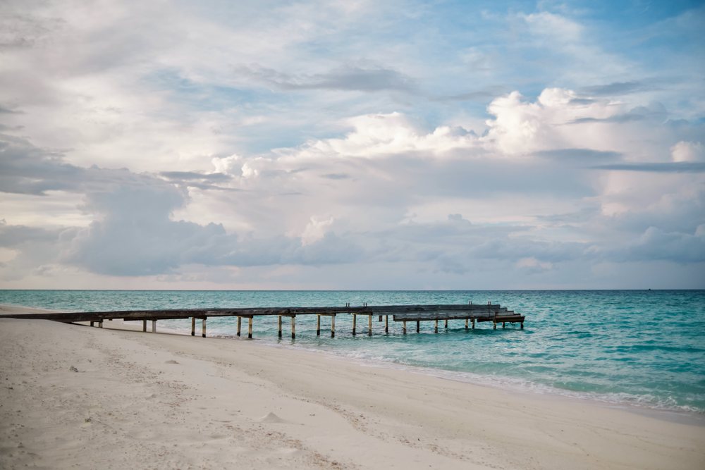 Wooden pier on a turquoise ocean beach with cloudy sky in a beach