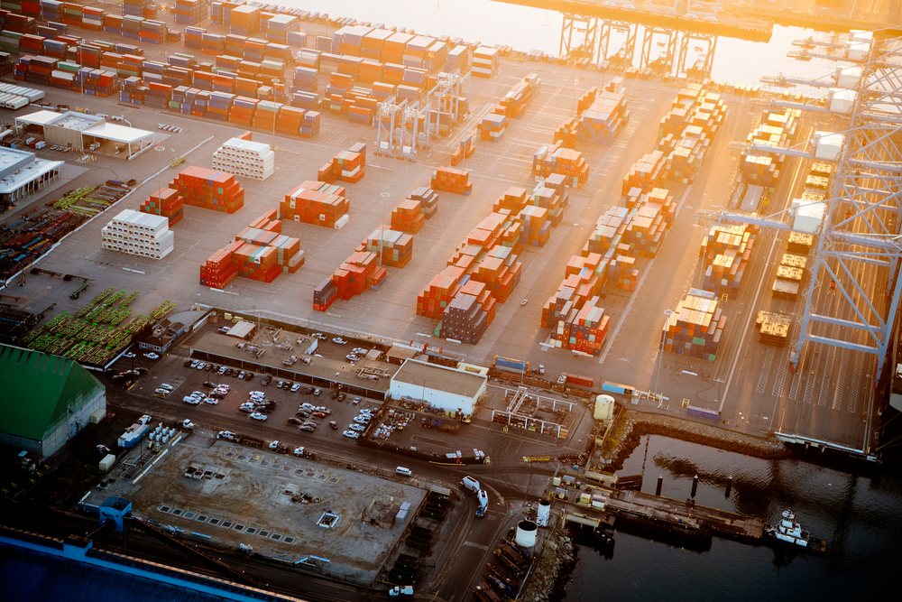 Cargo containers stacked at a major container yard during sunset with cranes and docks visible, a major container yard, CA, USA.