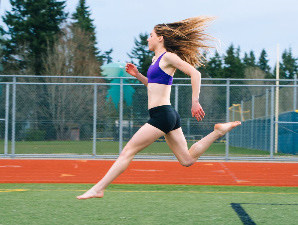 Woman runs barefoot on an outdoor athletic track, USA.