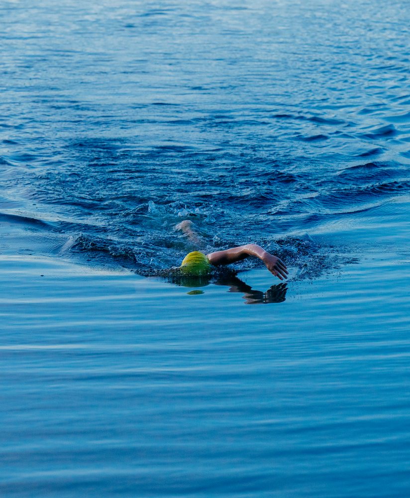 Swimmer wearing a yellow swimming cap performing freestyle stroke in an open water lake, USA.