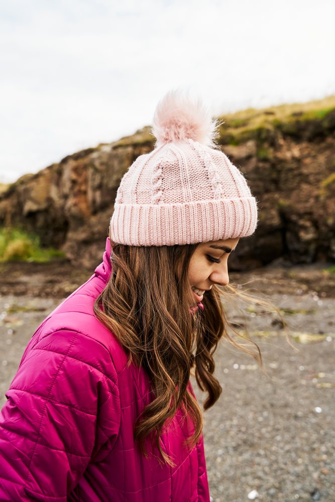 A white woman smiles outside wearing a pink hat and jacket