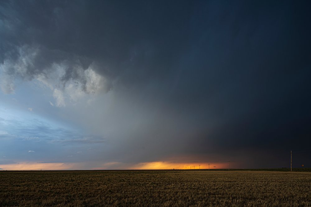 Storm clouds gather above an open field with power lines at sunset, located in Tornado Alley, Storm Chasing, Weather, Environment, Ulysses, Kansas, USA.