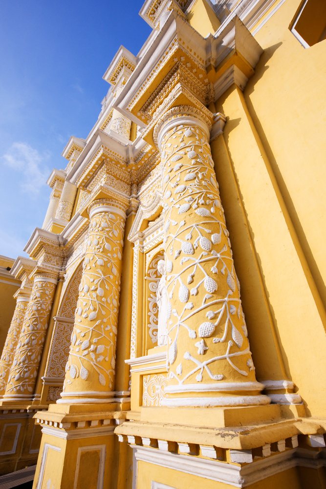 Iglesia La Merced church facade features ornate yellow and white baroque columns, Guatemala under a blue sky, Sacatepequez Department.
