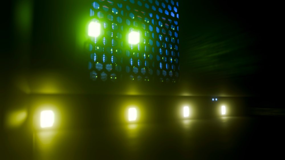LED light panels with blue, green, and yellow illumination form a hexagonal digital grid pattern in a dark room reflecting on a flat surface.