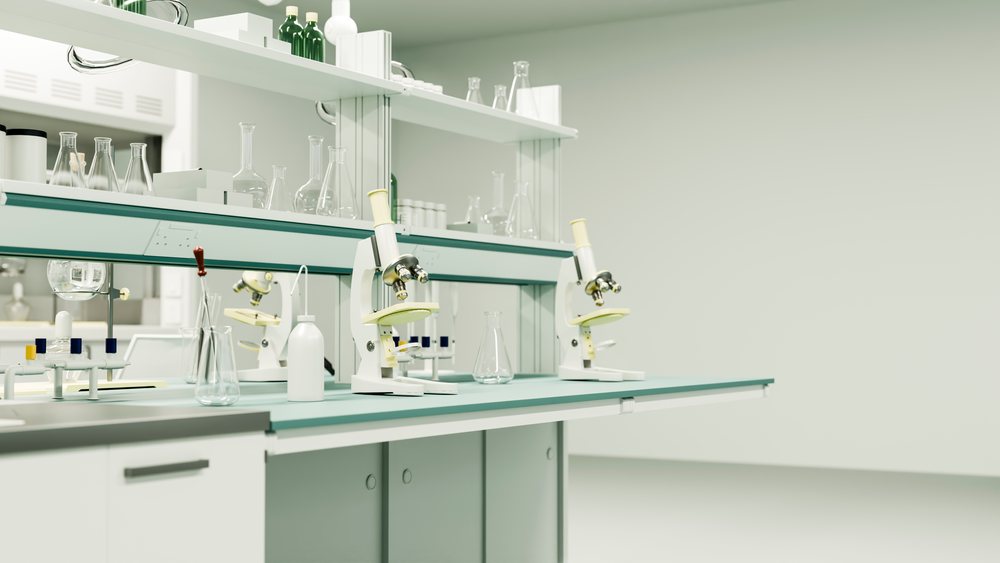 Microscopes and various laboratory glassware such as chemical flasks and bottles are arranged on laboratory countertops and shelves in a clean, sterile research environment.