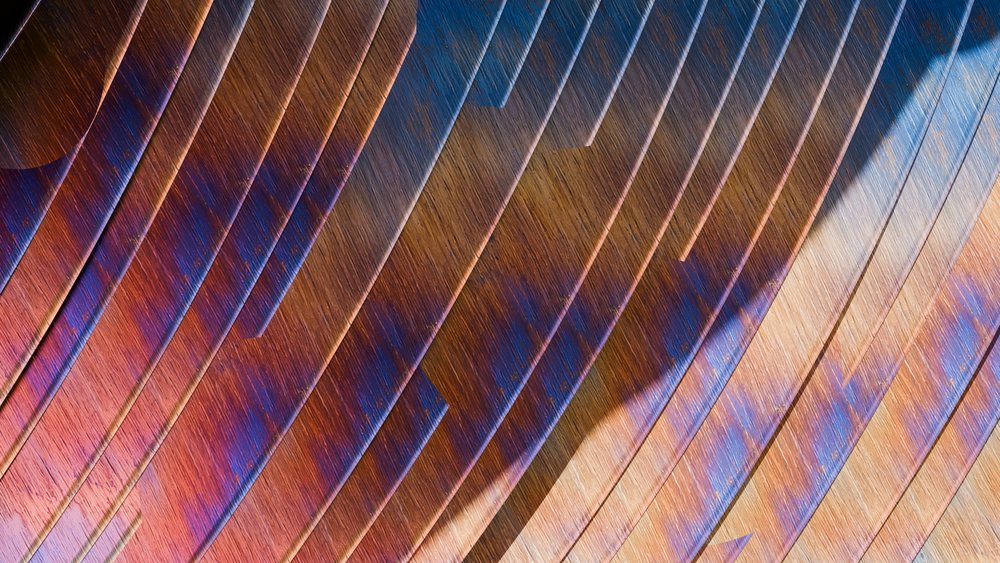 Wooden planks with colorful blue and orange stains form an abstract diagonal pattern, displaying visible wood grain and subtle light shadows.