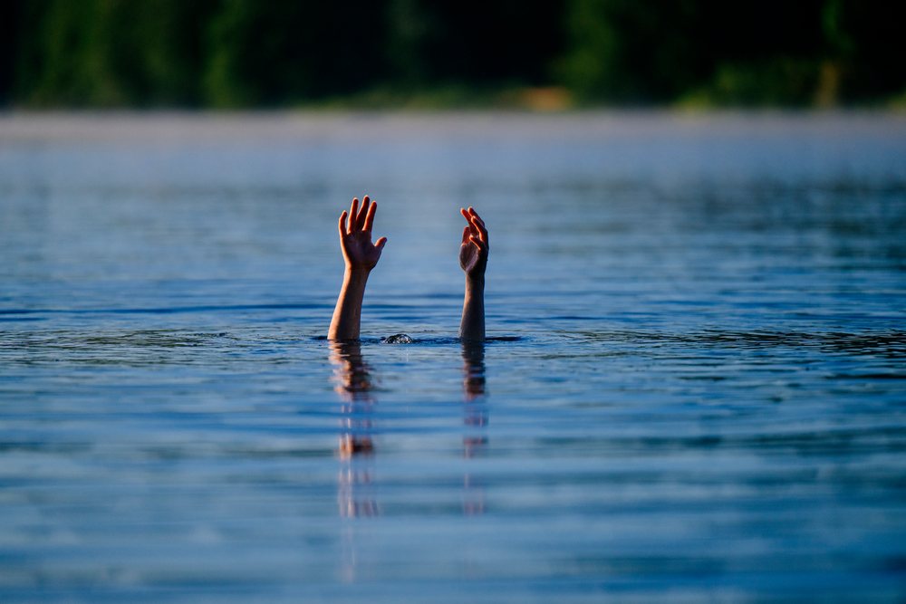 Hands raised above the water surface signaling distress in a calm lake, USA.