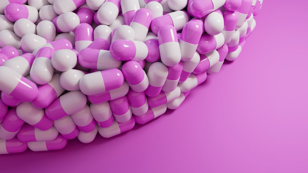 Pile of pink and white capsule pills on a pink background.
