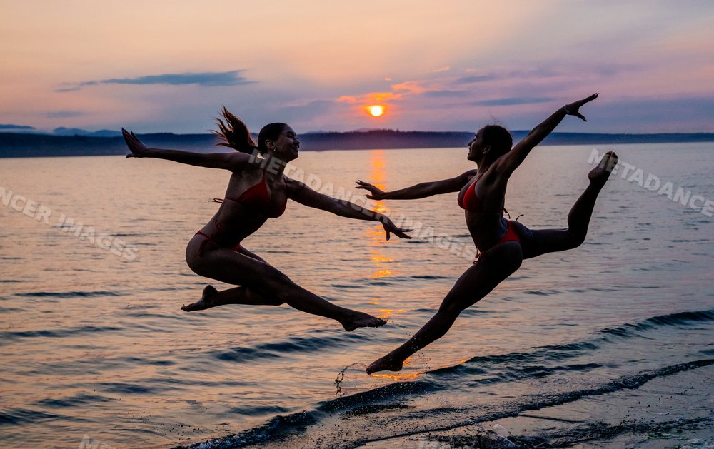Two women performing partner acrobatics yoga at sunset on a beach