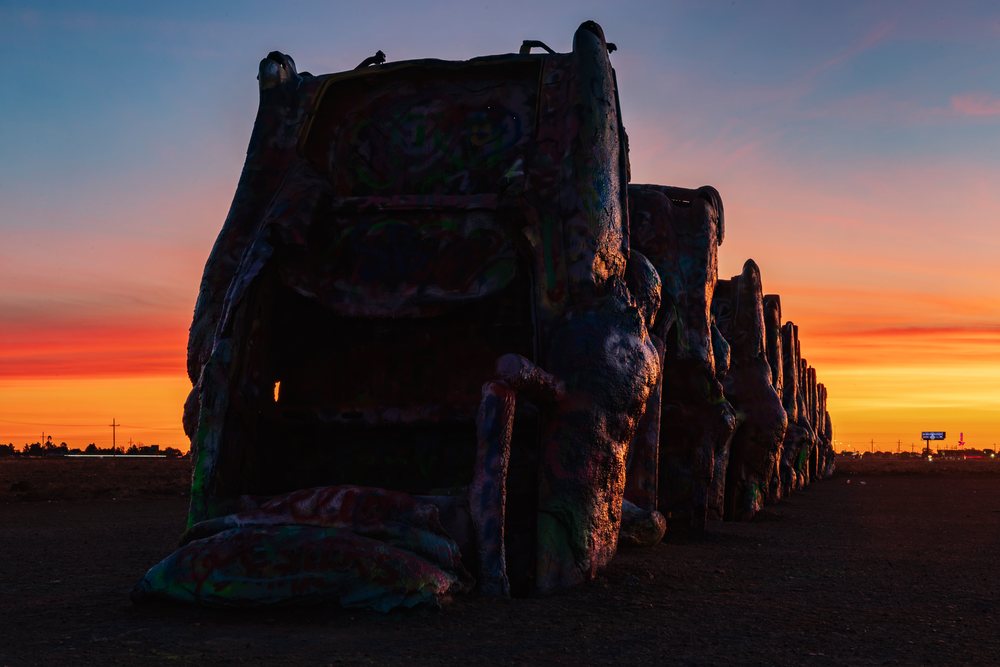 Vintage Cadillac cars buried nose-down in a row silhouette against a vibrant orange and pink Sunrise sky, Texas USA Route 66, Americana, Historic, Amarillo.