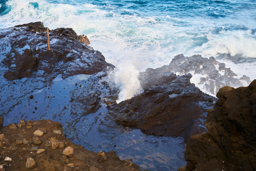 Ocean waves crash and splash against dark lava rocks along the rocky coastline of, Oahu, Hawaii, USA.